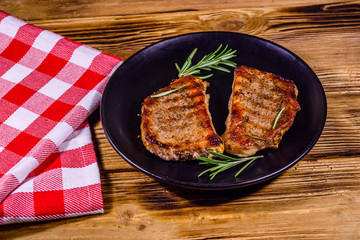 Plate with roasted steaks and rosemary twigs on a wooden table