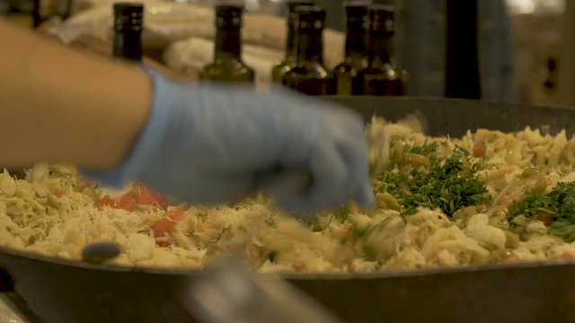 Cook pours parsley on top of a paella. Street foof market.