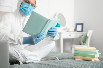 Man in biohazard suit reading book at home