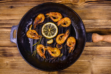 Roasted shrimps with lemon slice, garlic and rosemary in a cast iron pan. Top view