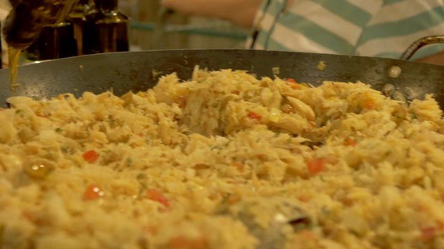 Cook pours olive oil on top of a paella. Street foof market.