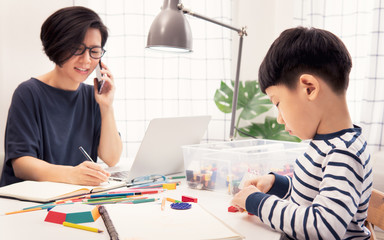 Social distancing & Work from home, Homeschool Asian little boy draw and color while stressed mother on phone, look at computer laptop working during pandemic of Covid-19, quarantine and city lockdown