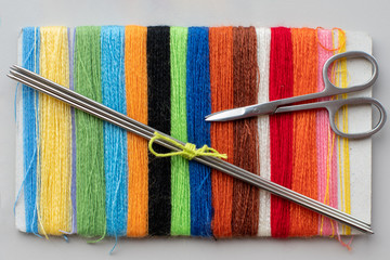 Close-up of multi-colored threads, knitting needles and scissors, top view. The concept of hobbies,...