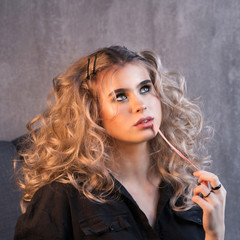 Portrait of a blonde girl with long and volume shiny wavy hair with chewing gum in her mouth. A woman is chewing gum. Stretching bubble gum.