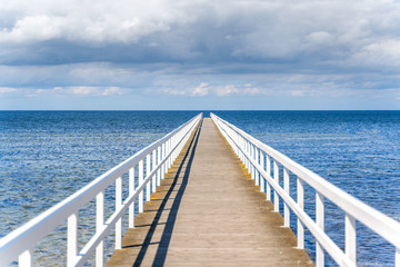 Fototapeta na wymiar Wooden white bridge to the sea with dramatic sky view over the long jetty.