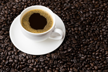 Hot black coffee with foam in a white coffee cup on coffee beans field background
