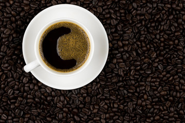 Hot black coffee with foam in a white coffee cup on coffee beans field background
