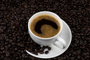 Hot black coffee with foam in a white coffee cup on coffee beans field background