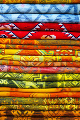 Stack of colored carpets and clothes shown in carpet shop. Rainbow colors
