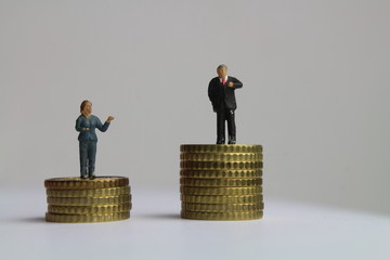 kleine Figuren auf unterschiedlich hohen Münzstapeln stehen für die ungleiche Bezahlung von...
