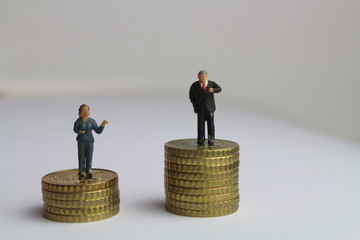 kleine Figuren auf unterschiedlich hohen Münzstapeln stehen für die ungleiche Bezahlung von...