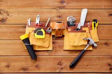 repair, building and renovation concept - belt with different work tools in pockets on wooden boards background