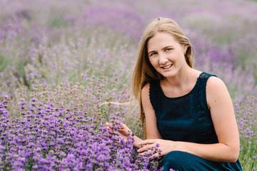 Beautiful girl in dress in purple lavender field. Beautiful woman walk on the lavender field. Girl collect lavender. Enjoy the floral glade, summer nature. Natural cosmetics and eco makeup concept.