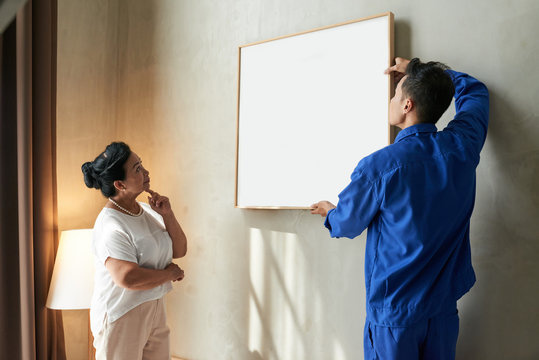 Handyman helping senior woman to hang picture on the wall in her apartment