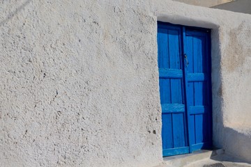 Shot of a typical rectangular Greek door made out of wood and painted in a vivid blue with a white roughcast wall on the side and a small step in front of it