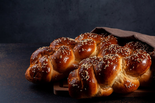 Homemade Challah -  special bread in Jewish cuisine.Main ingredients are eggs, white flour, water, sugar, salt  and yeast. Decorated  with sesame and poppy seeds. Dark background.