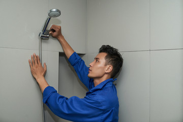 Plumber in uniform using wrench when installing shower head in bathroom