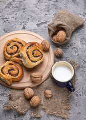 Basket of homemade buns with jam, served on old wooden table with walnuts and cup of milk