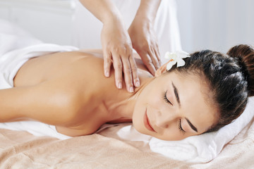 Smiling young woman enjoying relaxing neck and back massage in spa salon