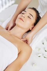Smiling young woman enjoying relaxing shoulder massage in spa salon