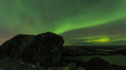 Northern lights over tundra and rocks.