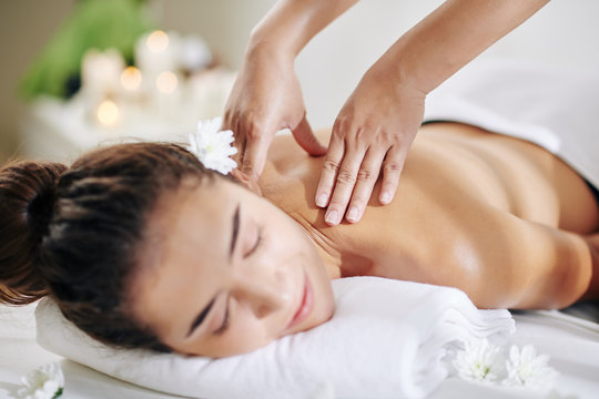 Close-up image of masseuse massaging neck and shoulders of young pretty woman