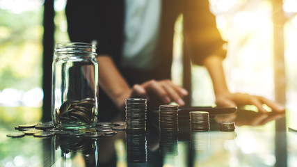 Closeup image of a businesswoman calculating with coins stack and a glass money jar for saving and financial concept