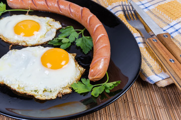 Fried eggs and wiener on black dish, fragment close-up