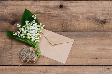 A bouquet of lilies of the valley tied with twine next to a letter envelope on a wooden background