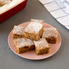 Homemade Tasty Applesauce Cake on a pink plate on a gray surface, side view.