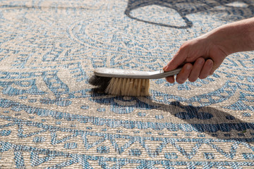 Man brushing an outdoor rug in a garden with a hand brush.  Grey and blue design
