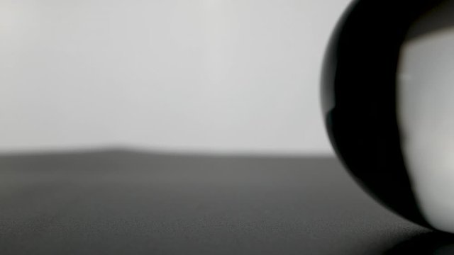 Crystal glass ball sphere transparent rolling on grey gradient background.
