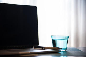 Laptop with turquoise glass of water and pen on wooden table