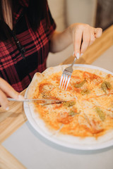 young beautiful girl cuts pizza with tomatoes and pepper in a cafe, girl's hands, fresh pastries with cheese, view from the top