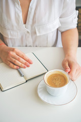 girl makes notes in a notebook, next is a coffee mug