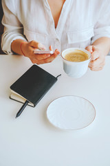 Obraz na płótnie Canvas girl in a black jacket holds a phone and a mug of coffee in her hand