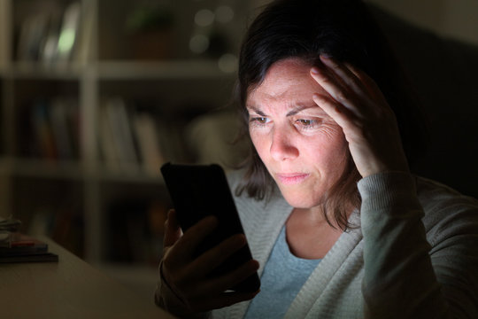 Preoccupied adult woman reading on phone at night at home