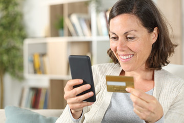 Happy adult woman paying with card on phone at home