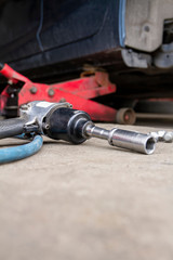 Pneumatic wrench tool on the asphalt and a car jack for lift up the body and changing the tire. Car without wheel