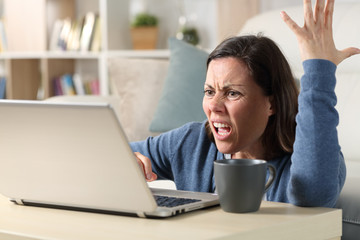 Angry adult woman watching video on laptop at home