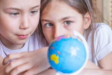 Child girl are sitting at home and looking at the globe, dreaming about traveling around the world.