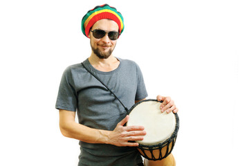 Young caucasian smiling man in rasta hat, sunglasses and grey t-shirt on white background with...