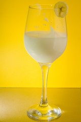 Photo of a banana flying into a glass of banana smoothie with milk and mint on a yellow background