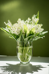 Bouquet of lilies of the valley in a glass vase on a green background