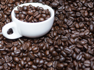 Close-up shot of a pile of roasted coffee beans with a white ceramic cup, stoneware or porcelain cup. Organic roasted coffee beans.