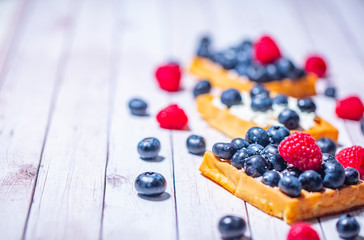 Sweet Homemade waffles with fresh raspberries, blueberries and cream on pink background