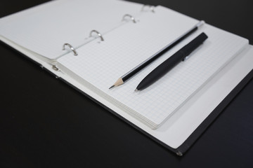 Open diary with a pencil and a black pen on a black wooden table