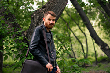 A bearded Irishman in a leather jacket makes faces in the middle of the forest.