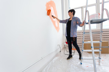 Repair in the apartment. Happy middle-aged woman paints the wall with paint. Copy space.