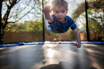 Cute little boy jumping on the trampoline like a superhero, people enjoy life after lockdown